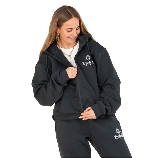 Frau steht mit Händen in den Taschen einer dunkelgrünen Jogginghose mit Krombacher-Logo, trägt weiße Crop-T-Shirt, dunkelgrünen Jacke