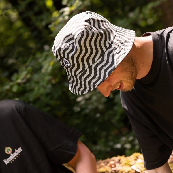 Mann mit grün-weiß gestreiftem Bucket-Hat und schwarzem T-Shirt lehnt sich nach vorne