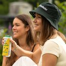 Zwei lächelnde Frauen sitzen im Freien, eine trägt einen dunkelgrünen Bucket Hat mit weißem Krombacher Logo und hält eine Dose Krombacher Radler