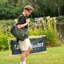 Junger MJunger Mann mit Sonnenbrille trägt zusammengeklappten Krombacher Liegestuhl und grüne Tasche in Parkanlage neben Teich