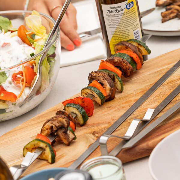 Gemüsespieß mit Zucchini, Paprika und Champignons auf einem Holzbrett neben einem Salat in Glasschüssel und einer Flasche Krombacher Radler 0,0