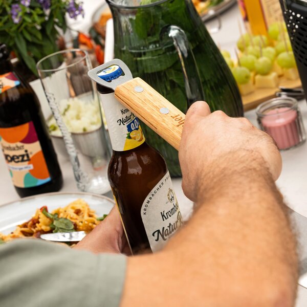 Hand öffnet mit einem Holzflaschenöffner eine Flasche Krombacher Naturtrüb 0,0.
