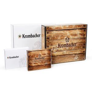 Verschiedene Geschenkboxen in zwei größen und Varianten. Vier Krombacher Geschenkboxen in verschiedenen Größen, zwei mit Holzoptik und Aufschrift 'Krombacher Brautradition seit 1803', zwei weiße mit Krombacher-Logo.