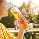 Frau hält ein Krombacher Weizenglas, im Freien bei Sonnenschein.