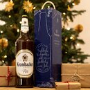 3-Liter Magnumflasche Krombacher Pils neben blauer Geschenkbox mit Weihnachtsgruß vor geschmücktem Weihnachtsbaum und verpackten Geschenken.