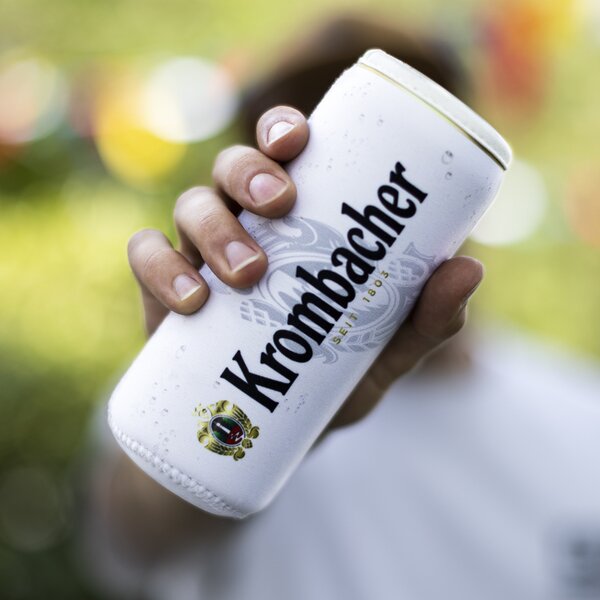Hand hält eine weiße Krombacher Bierdose mit Dosenkühler inklusive Krombacher Logo.